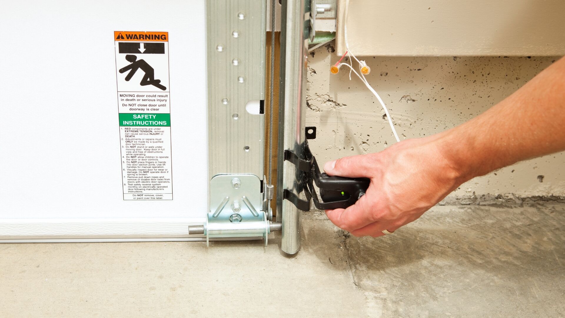 A homeowner fixing a safety sensor on their garage door