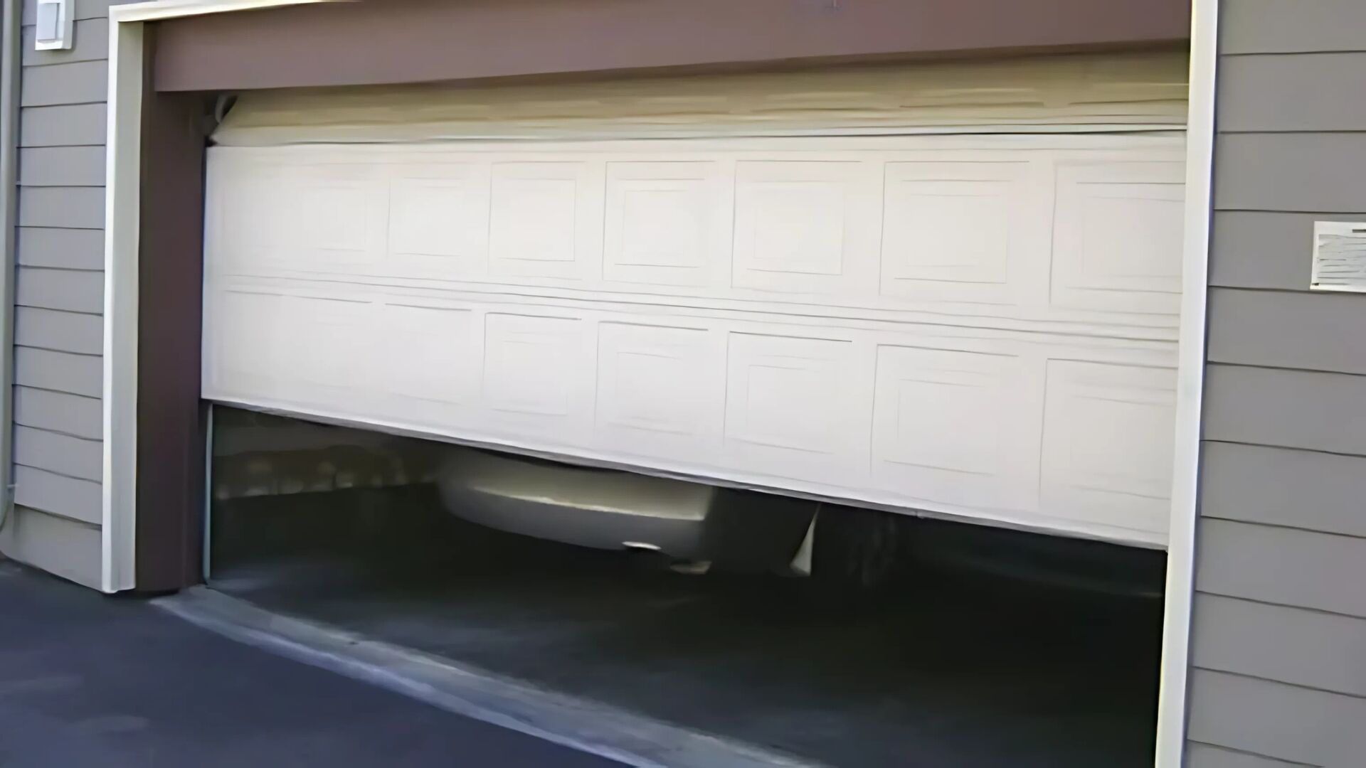An overhead door stuck midway, with a car trapped inside, requiring garage repair service